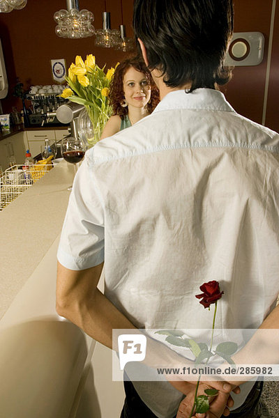 Mann schaut Frau an,  die Rose hinter dem Rücken hält.