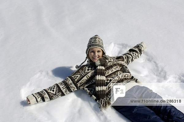Junge Frau auf Schnee liegend  lächelnd  Portrait