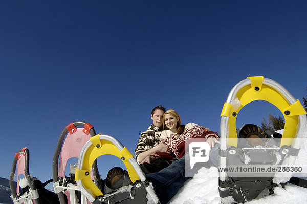 Junges Paar im Schnee sitzend mit Schneeschuhen  Tiefblick