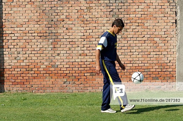 Junger Mann Jonglieren Soccer Ball an die Wand