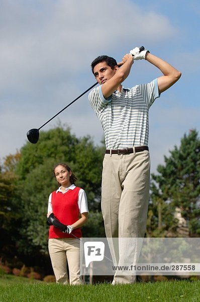 Man hitting a golf shot with a woman looking on