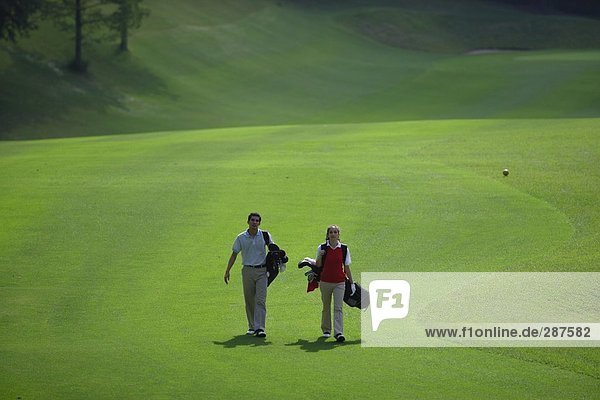 Paar zu Fuß auf dem Fairway trägt ihre Golfbeutel