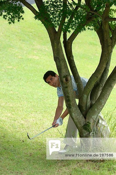 Mann eine Schuss hinter einem Baum Golf zu spielen