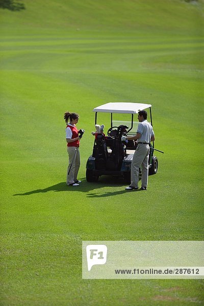 Paar hält Golfclubs in der Nähe ein Golf-Cart stehen
