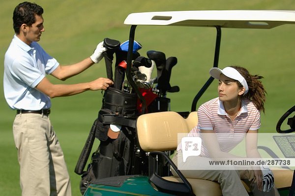 A male golfer selects a club while his partner is seated in their golf cart