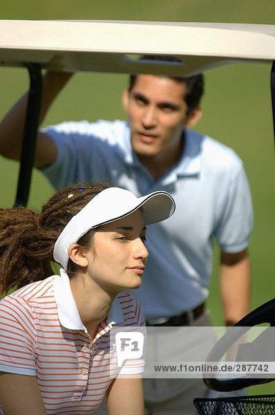 Side view of a woman sitting in a golf cart while a man is seen at the back