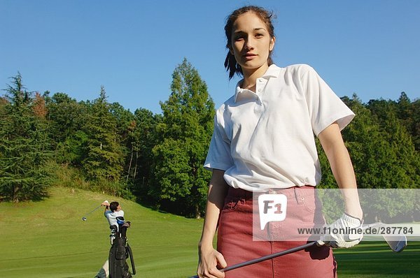 Female golfer smiling at the camera with a man in the background