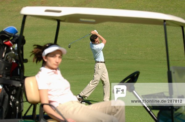 Weibliche Golfer fangen einige Sonnenschein während ihr Partner ein Schuss spielt