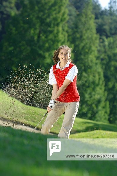 A female golfer looks up after making a bunker shot