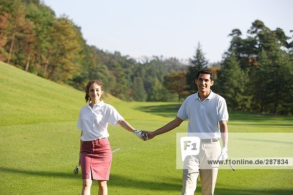 Couple holding hands as they walk down the fairway