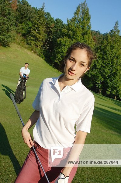 Weibliche Golfer posiert mit ihrem Partner im Hintergrund