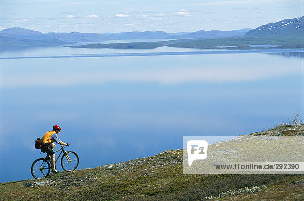 A man on a bicycle by a lake.
