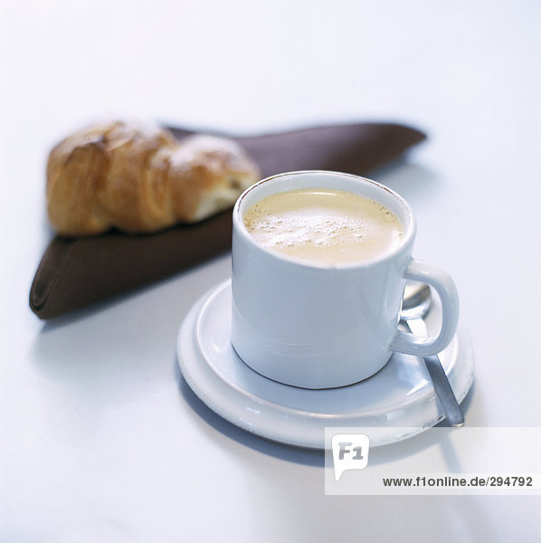 Eine Tasse Kaffee und einem Croissant im Hintergrund.