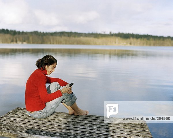 Eine Frau mit einem Mobiltelefon sitzen auf einer Brücke.