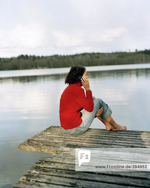 A woman sitting on a bridge talking on a mobile phone rear view.