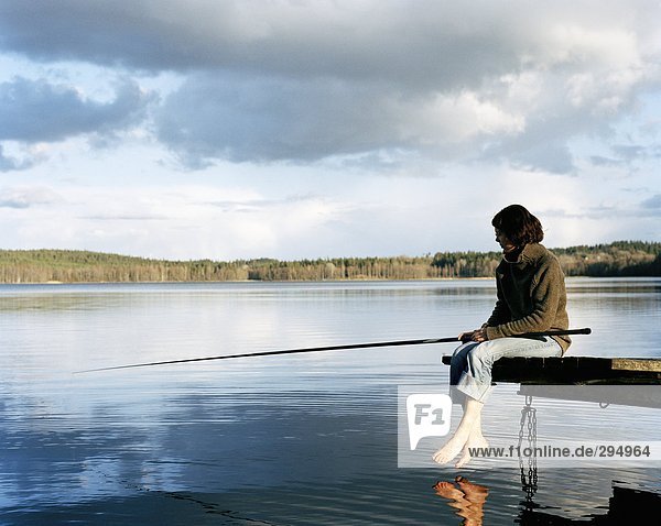 A woman sitting on a bridge fishing.