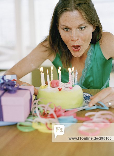 Eine Frau Ausblasen Kerzen auf einem Geburtstagskuchen.