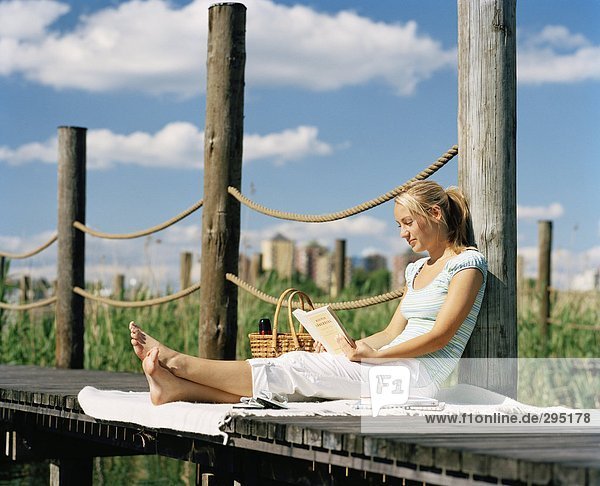 Eine Frau sitzt auf einer hölzernen Brücke ein Buch zu lesen.