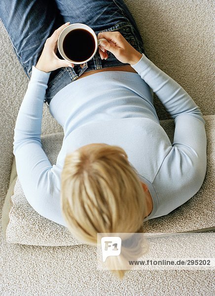 Eine Frau in einem Sofa halten eine Kaffeetasse fotografiert von oben sitzen.