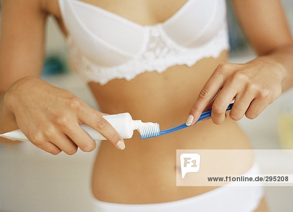 Eine Frau gekleidet in Unterwäsche  Zahnpasta auf eine Zahnbürste.