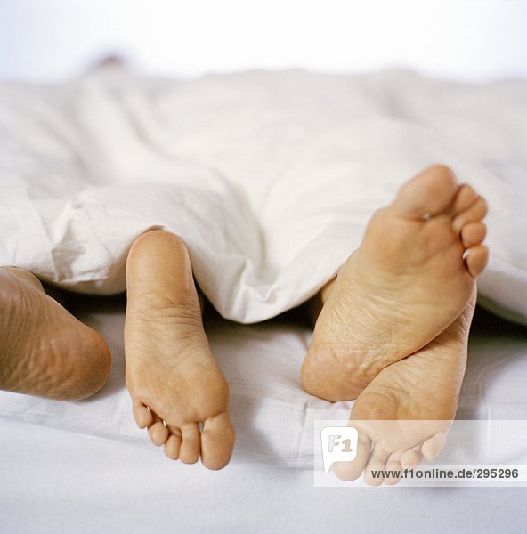 Nackte Füße aus einer Sammelfläche auf einem Bett Herauslehnen.