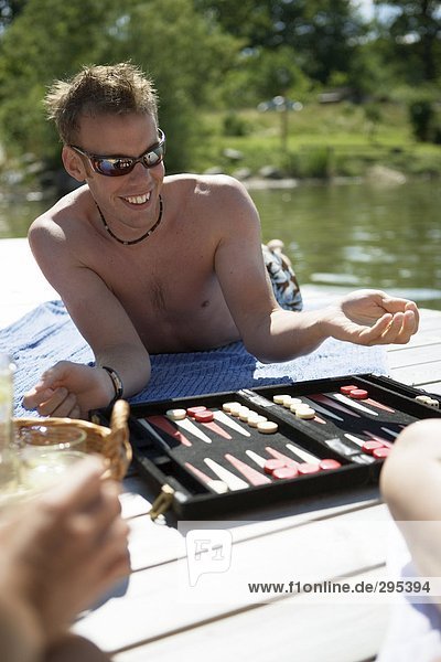 Ein Mann in Sonnenbrillen liegend auf einer Brücke spielen Backgammon.