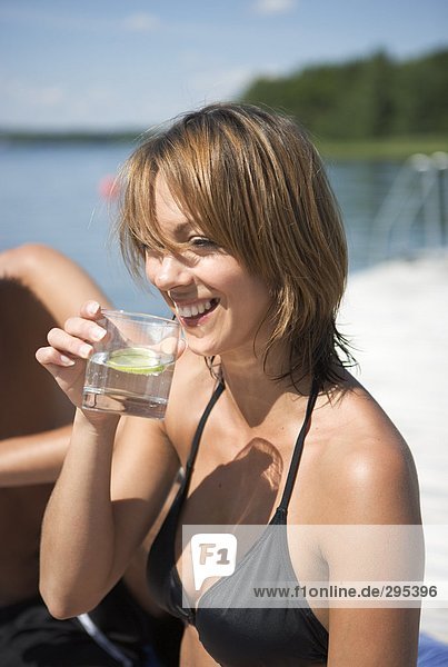 Eine Frau in einem Bikini sitzen auf einer Brücke aus einem Glas trinken.
