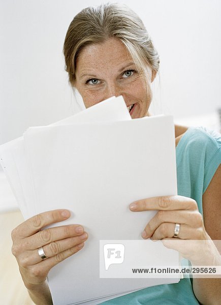 Einer blonden Frau hält Papiere an ihr Gesicht.