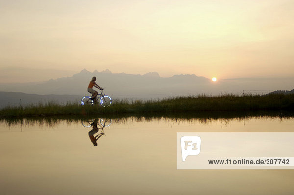 Österreich  Alpen  Frau mit dem Fahrrad am See  Seitenansicht