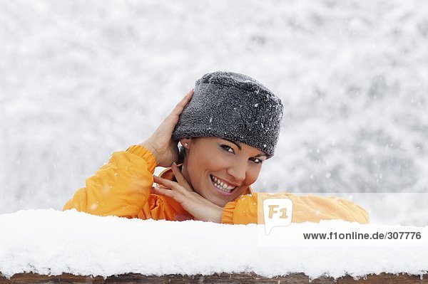 Junge Frau im Schnee auf Holzgeländer gestützt