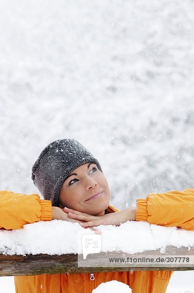 Young woman in snow  leaning on wooden railing