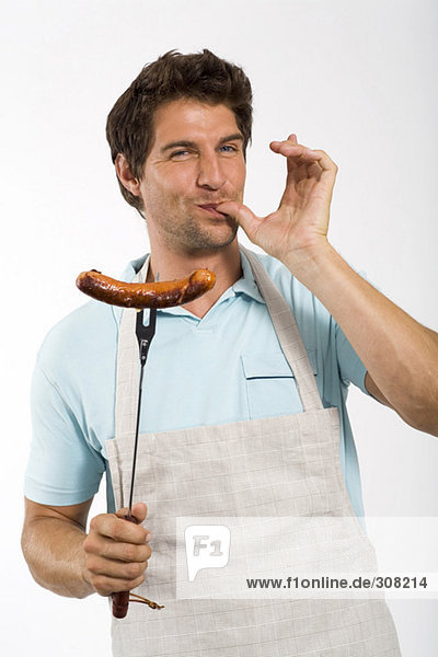 Junger Mann mit Grillwurst auf Gabel  Portrait