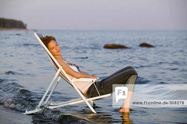 Junge Frau im Liegestuhl am Strand  Seitenansicht