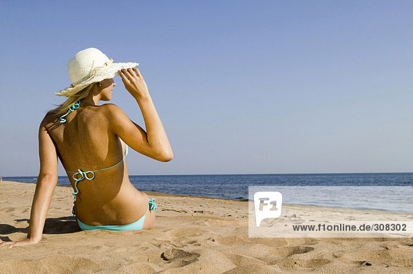 Junge Frau am Strand sitzend  Rückansicht