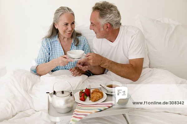 Erwachsenes Paar auf dem Bett sitzend mit Frühstück  lächelnd