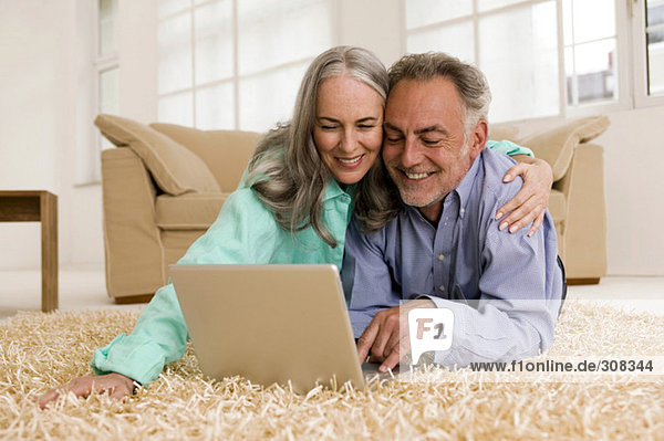 Ein reifes Paar auf dem Teppich liegend  mit Laptop  lächelnd