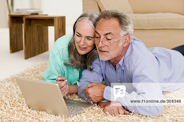 Mature couple in living room  lying on floor with laptop