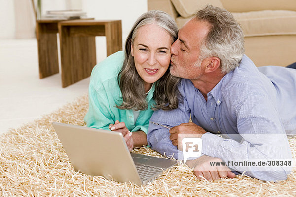 Erwachsenes Paar auf Teppich liegend mit Laptop  Mann küssend Frau