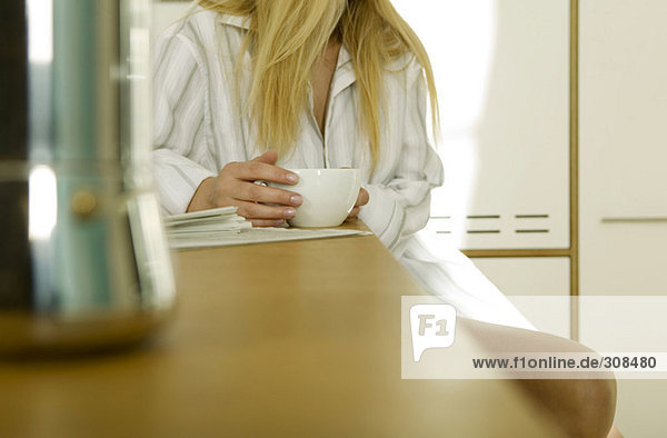 Junge Frau in der Küche sitzend mit Tasse Kaffee  Mittelteil