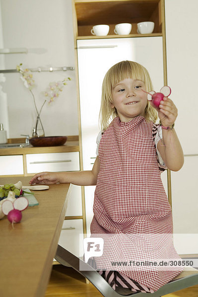 Girl (4-5) in kitchen  holding radish  close-up