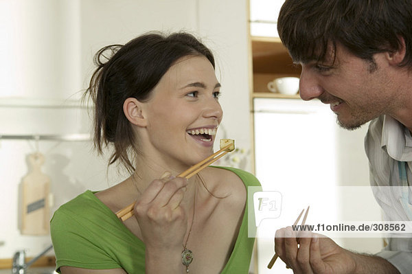 Junges Paar isst mit Essstäbchen  lächelt.