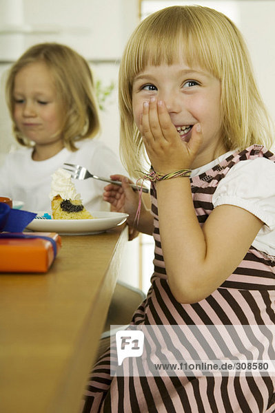 Two girls (4-5) eating cake in kitchen