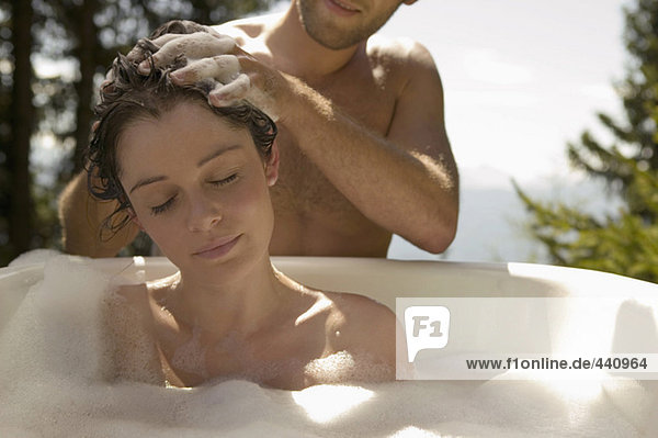 Young woman lying in bathtub  young man washing hair