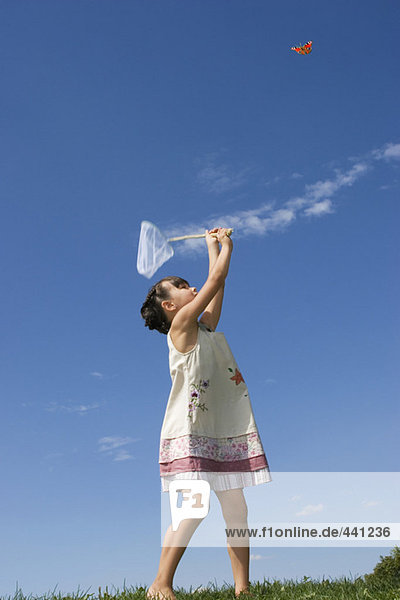 Girl (7-9) holding net  trying to catch butterfly