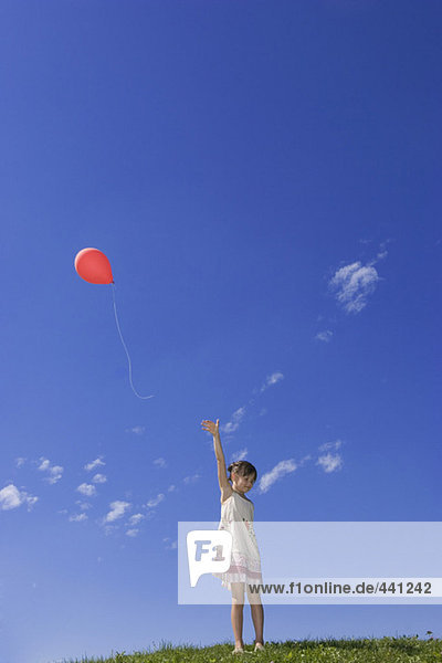 Girl (7-9) standing in meadow,  releasing balloon