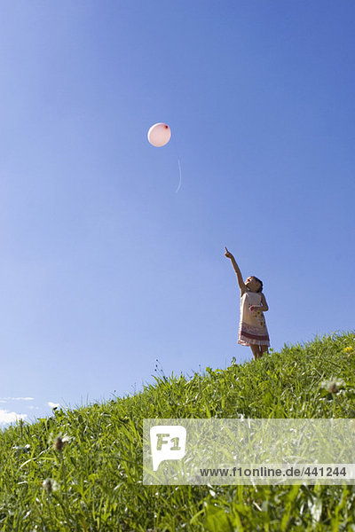 Mädchen (6-7) steht auf der Wiese und zeigt auf den Ballon in der Luft.