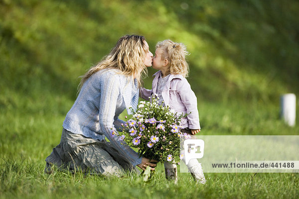 Mutter küsst Tochter  hält Blumenstrauß  Seitenansicht