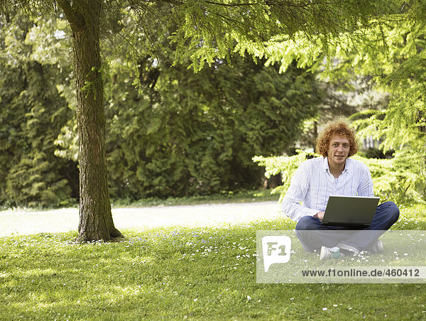 Ein Mann mit einem Laptop auf eine Wiese.