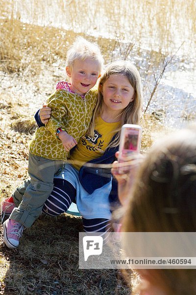 Girl photographing her siblings with her cellphone.
