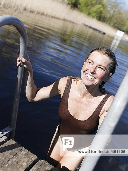 A woman coming up from a swim in a lake.